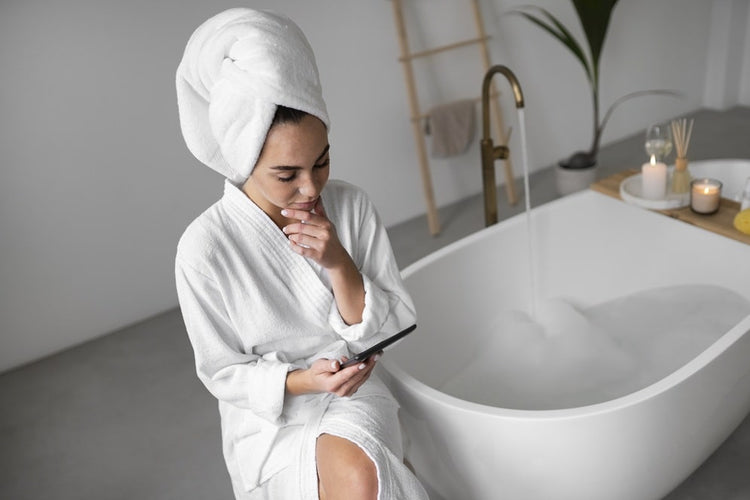 une femme assise a coter de sa baignoire enveloppé dans un peignoir dans une ambiance bien être.