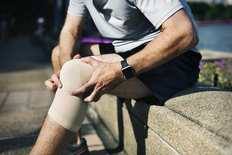 un homme assis sur un mur qui porte une genouillère de compression