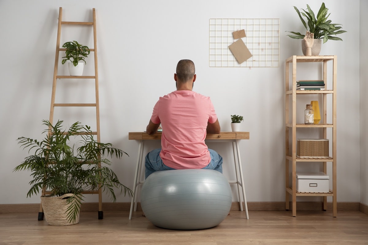 un homme assis présenté de dos assis sur une swiss Ball de rééducation dans un petit salon zen .