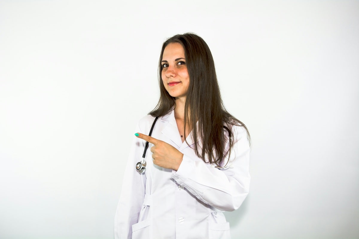 une femme médecin souriante qui pointe du doigt sur sa droite.