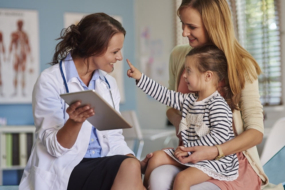 une femme médecin qui ausculte une petite filles assisse sur les genou de sa maman.